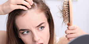 Perceber queda de cabelo dicas. Na foto a mulher está observando uma escova de cabelo cheia de fios