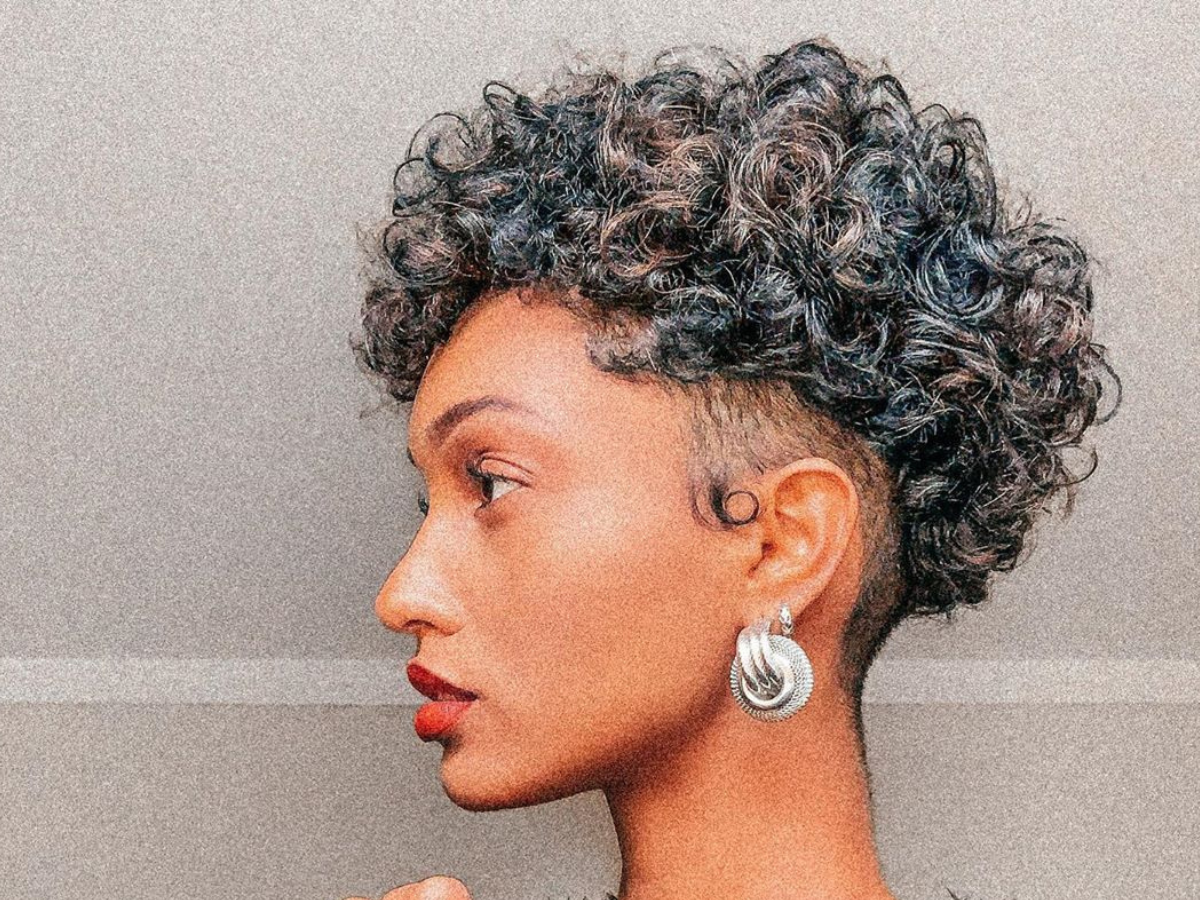 Corte pixie cut para cabelos cacheados. Foto mulher negra com pixie cut nos cachos virada de lateral