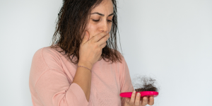 Dicas exclusivas queda de cabelo. Foto mostra uma mulher branca de blusa rosa segurando uma escova de cabelo cheia de fios