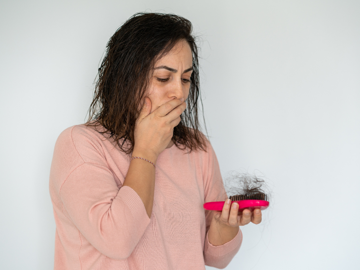 Dicas exclusivas queda de cabelo. Foto mostra uma mulher branca de blusa rosa segurando uma escova de cabelo cheia de fios