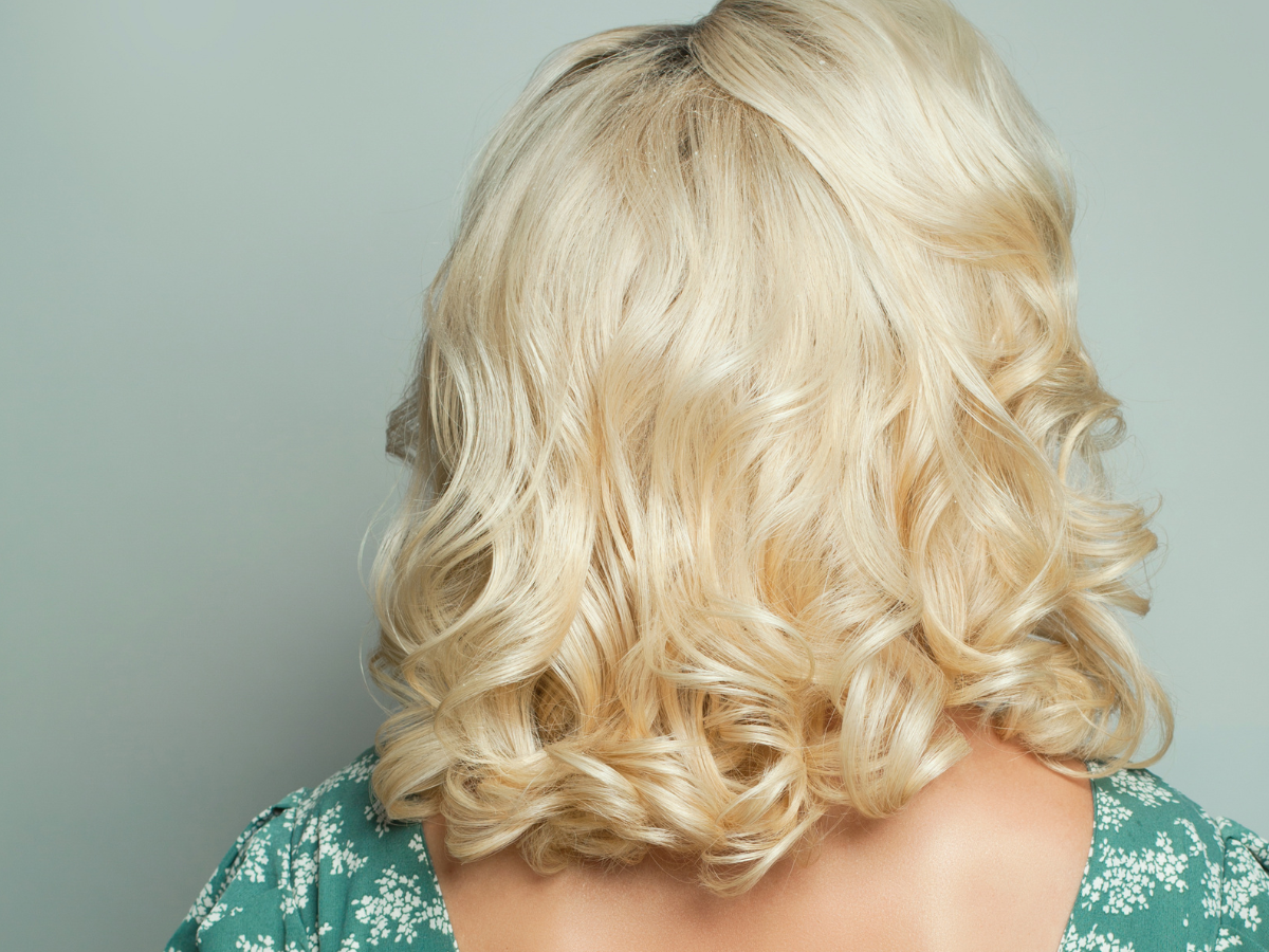 Long Bob: artistas com mais de 50 anos com o corte. Foto mulher loira de costas com o cabelo cacheado próximo aos ombros.