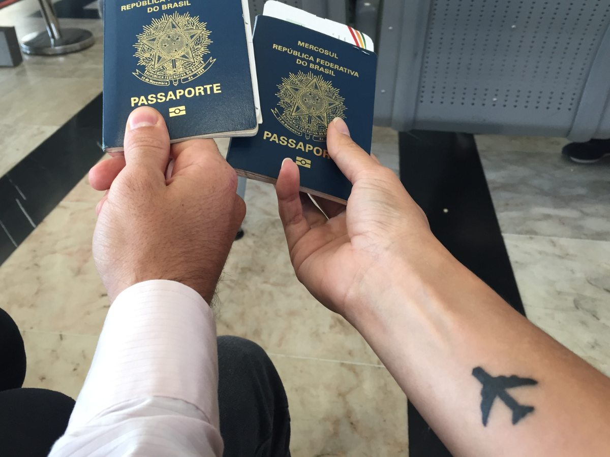 Tatuagens para quem ama viajar. Foto aparece dois braços segurando passaportes e um dos braços tatuado com um avião.