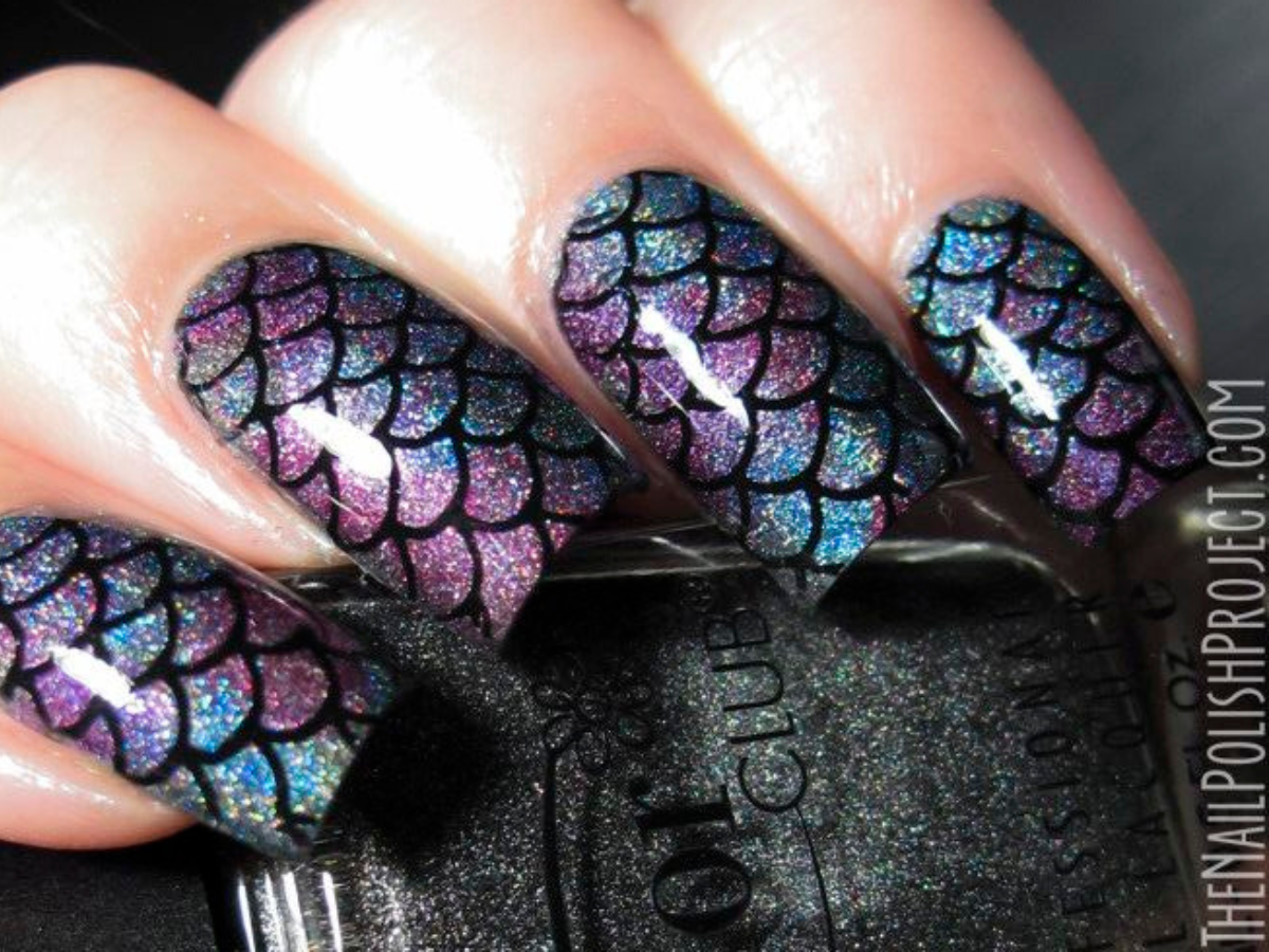 Unhas de Sereia- Pinterest. Foto mostra uma unha com esmalte roxo e azul com escamas de peixe em preto e brilho. Os dedos estão segurando um esmalte de cor preta brilhante