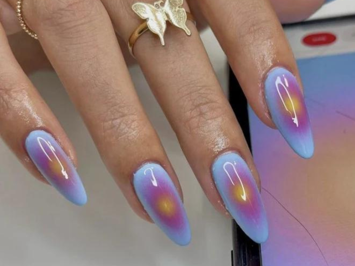 Aura Nails. Foto mostra unhas pintadas de azul claro e com a aura desenhada no centro da unha de rosa e amarelo.