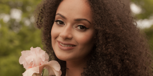 Cabelo crespo mentiras que já te contaram. Foto mostra uma mulher negra com cabelo crespo segurando uma flor rosa na mão.