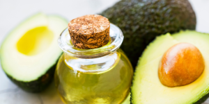 Óleo de abacate na pele e cabelo. Foto mostra uma embalagem de vidro com óleo e a fruta abacate ao lado.