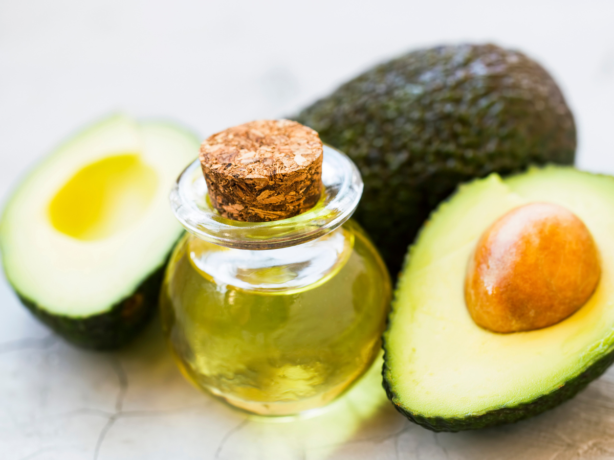 Óleo de abacate na pele e cabelo. Foto mostra uma embalagem de vidro com óleo e a fruta abacate ao lado.