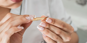 Unha postiça colada com Tekbond. Foto aparece mulher passando cola em uma unha postiça decorada de branco