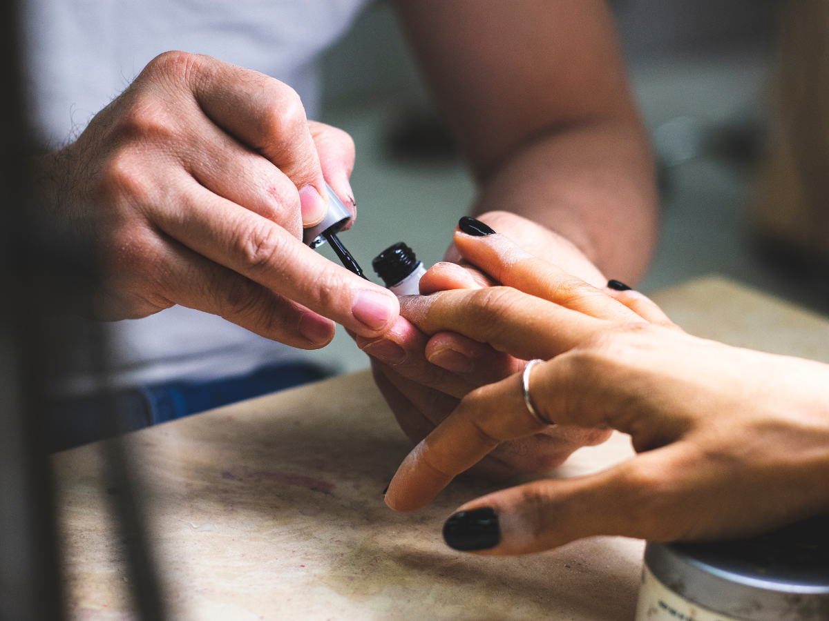 Dicas para fazer com que o esmalte dure mais. Foto mostra mão tendo as unhas pintadas de preto