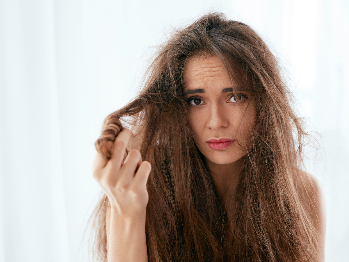 Cabelos Porosos máscaras para tratamento. Foto traz mulher com cara de preocupada segurando o cabelo liso danificado de cor castanho.