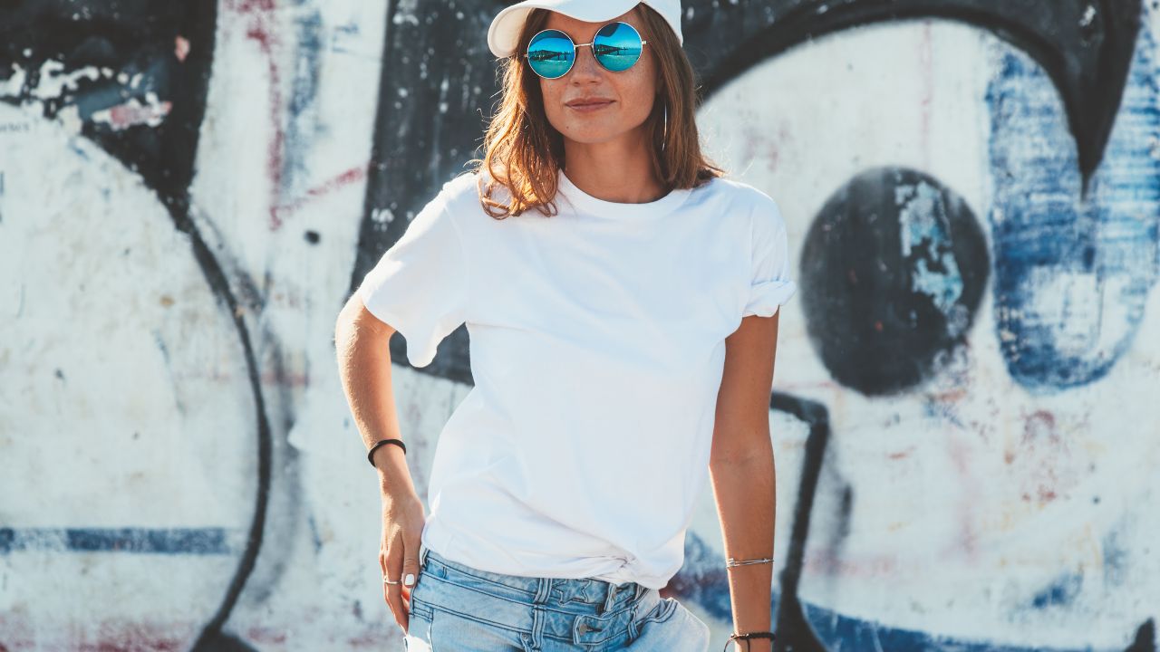 mulher com camiseta branca, jeans, boné branco e óculos de sol