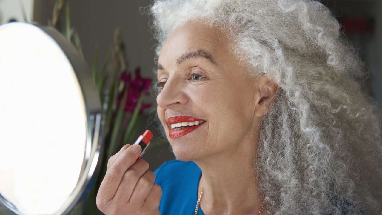 mulher madura de cabelo grisalho aplicando batom