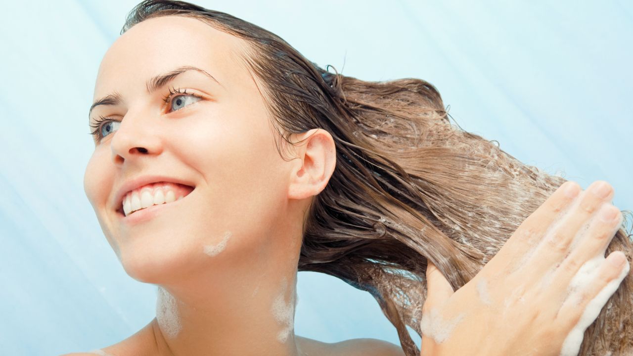 mulher sorrindo enquanto lava o cabelo